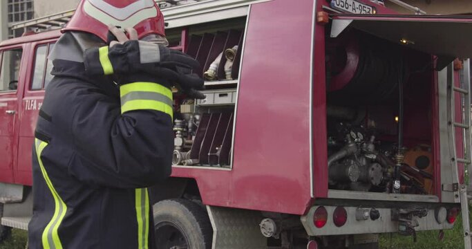 Firefighter with protective uniform and helmet stand in front of fireman rescue truck while preparing equipment.