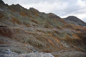 Alpine hills of rocks and stones. Some yellow mosses and lichens. Cloudy sky.