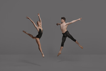 Fototapeta na wymiar Young man and woman, ballet dancers performing isolated over dark grey studio background. Expressing talent