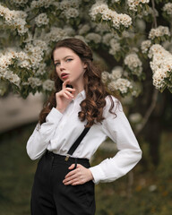 
A thoughtful girl in a strict outfit on the background of a blooming garden