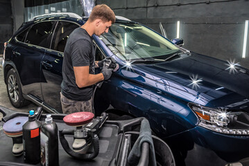 Plakat Professional car service male worker, with orbital polisher, polishing blue luxury car hood