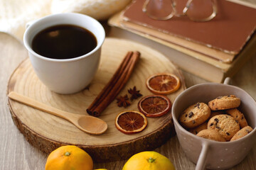 Cup of tea or coffee, various spices, bowl of cookies, tangerines, books, reading glasses and knitted blanket on wooden table. Hygge at home concept, selective focus.