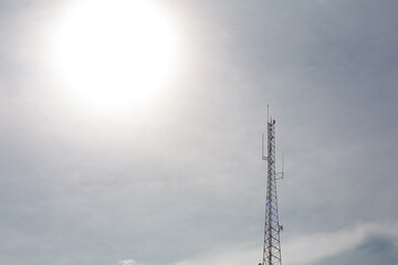 A radio or telephone tower in a backlit sky with the sun in the background.