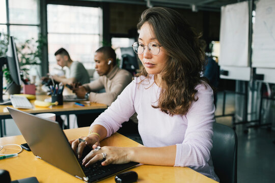 Female computer programmer coding on laptop at desk in startup company