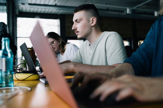 Concentrated businessman working on laptop amidst colleagues in startup company