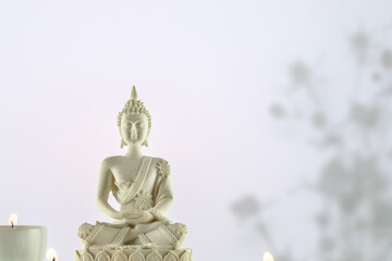Buddhism composition with white Buddha statue and candles on a white background with shadows and copy space. Vesak, Buddha Day. Mental health, relax, yoga and meditation. Soft image style