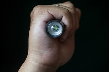 An LED flashlight held in a person's hand on a black background.