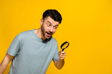 Photo of positive stylish man hold magnifying glass interested look empty space advert sale discount isolated on yellow color background
