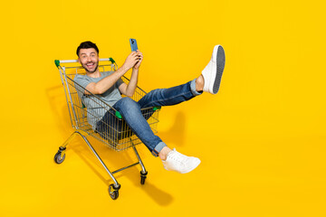 Full body portrait of positive funky person sitting market trolley hold telephone isolated on...