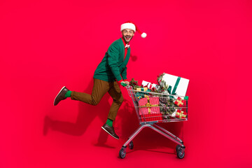 Full length photo of funny excited guy dressed xmas green cardigan buying noel gifts shoppers tray isolated red color background © deagreez