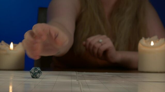 Woman Rolls Blue Twenty Sided Die Across Game Table with Candles Lit
