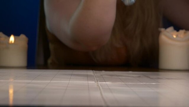Woman Rolls Grey Twenty Sided Die Across Game Table with Candles Lit