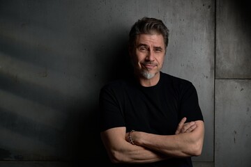 Portrait of happy casual middle aged, mid adult caucasian man in his 50s, smiling, standing against dark gray wall. . Copy space .