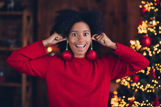 Portrait of excited funky small girl arms hold x-mas tree decor toys instead earrings enjoy festive magic indoors