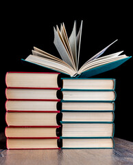 Naklejka premium Two stacks of hardcover paper books and one open.