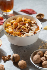 Healthy breakfast: caramelized apples oatmeal on the light grey background arounded by apples, nuts and autumn leaves. Close up