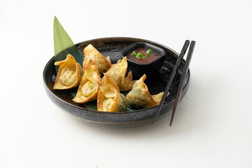 Black plate with gourmet fried dumplings and sauce on a white background
