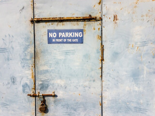 A No Parking sign outside a rusty locked metal door on a wall.