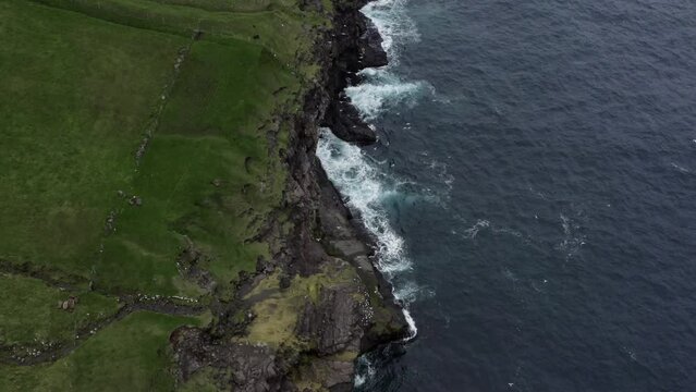 Aerial shot of a coastline at Faroe Island with waves hitting the cliffs