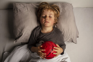Healthy child, sweetest blonde toddler boy sleeping in a football ball. Dream of becoming a football player. Young soccer player. Beautiful baby boy have a healthy sleep in the bed. Sleeping baby.