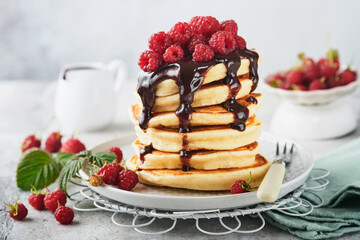 American pancakes. Stack pancakes with fresh raspberry with chocolate glaze or toppings in white bowl on light gray table background. Homemade classic american pancakes. Magazine concept. Top view.