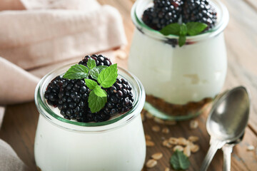 Yogurt with granola, blackberry berry fruits and muesli served in glass jar on wooden background. Healthy breakfast concept. Healthy food for breakfast, top view
