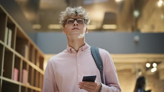 Portrait of a Young Caucasian Man Walking Across Corporate Office Hall, Browsing Web on his Smartphone and Smiling. Succesfull Entrepreneur Walks and Thinks of Startup Strategy. Slow Motion