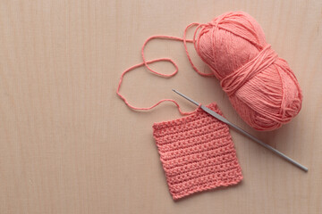 Crochet handmade square pattern, pink yarn coil, hook, knitting crocheting top view on a wooden background