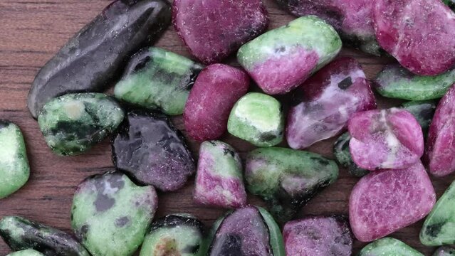 Ruby zoisite jewel stones heap up texture on brown varnished wood background. Moving right seamless loop backdrop.