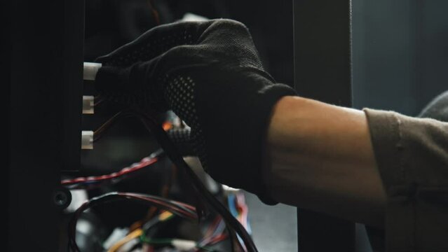 Close up of unrecognizable electrician in safety gloves connecting wires in server room