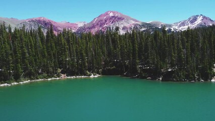 High-angle drone shot of a beautiful alpine Emerald lake in Colorado, a sunlit snowy forest near
