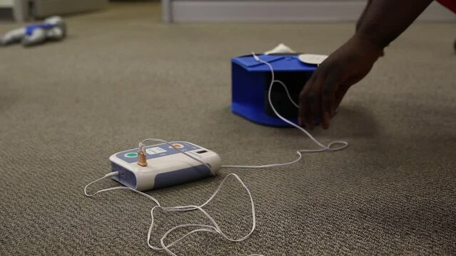 Person turning on an AED practice machine connected to an adult pad on the floor- concept of health
