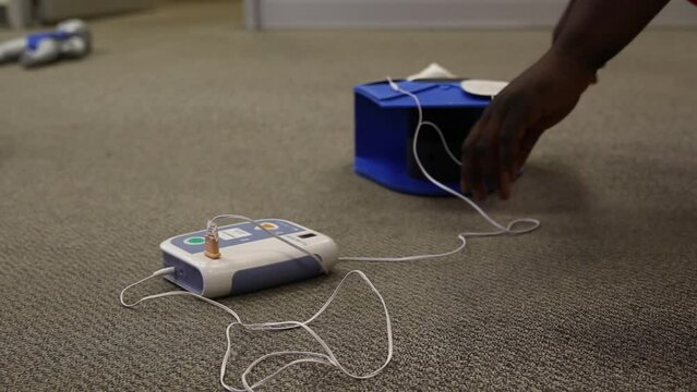 Person turning on an AED practice machine connected to an adult pad on the floor- concept of health
