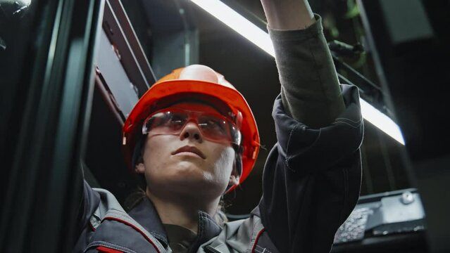 Focused female electrician in hard hat and safety glasses connecting cables in server room