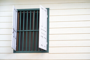 White folding wooden window with green steel grill protection on vintage wood wall in Thailand