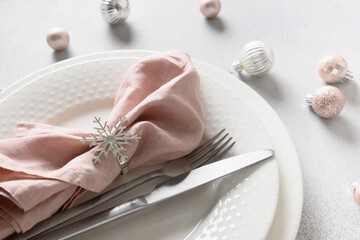 Christmas festive table setting with white plate, pink ball, and napkin ring as snowflake on gray background. Close up. Xmas dinner.