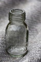 Small bottle with divisions and a carving on a neck on a gray wave background.