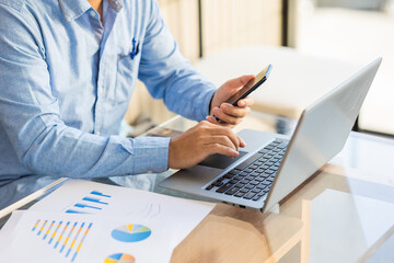 Asian businessmen use equipment for business. Holding a smartphone that works with laptops and mobile phones, showing statistics and software apps.