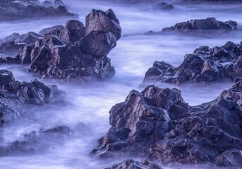 Long exposure of fog, mist encircling rocks, a purple background