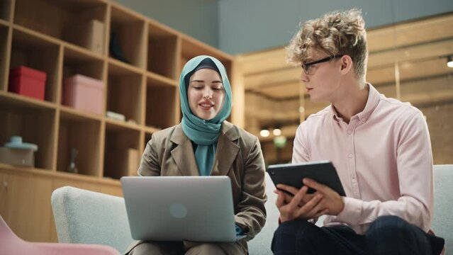 Two Creative Colleagues Discussing and Pointing at a Laptop in Modern Casual Office. Caucasian Male Sales Manager Discussing Project Plan on Tablet with Muslim Female Legal Assistant. Slow Motion