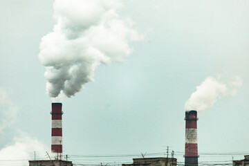 industrial chimneys with heavy smoke causing air pollution on the gray smoky sky background
