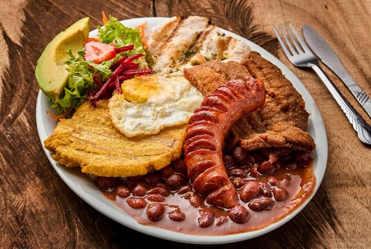 Top view of a white plate with Bandeja paisa with an egg, and vegetable salad on a wooden table