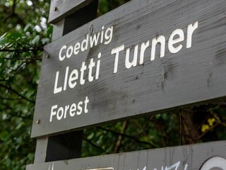 Fototapeta premium Low-angle shot of Lletti Turner Forest sign on a wooden board against green trees