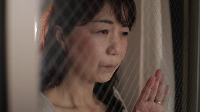 Asian lady looking outside through the window. Tired and sad face. Slow-mo.
