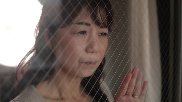 Asian lady looking outside through the window. Sad and painful face. Slow-mo.