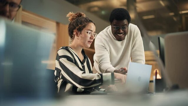 Portrait of Two Creative Young Colleagues Consulting Eachother Using Laptop in Modern Office. Black Male Supervisor Discussing Scheduling with Female Hispanic Head of Operations. Slow Motion.