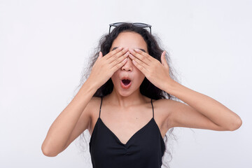 A young asian woman covers her eyes with her hands. Anticipating a surprise gift or hide and seek. Isolated on a white background. Spoiler alert concept.