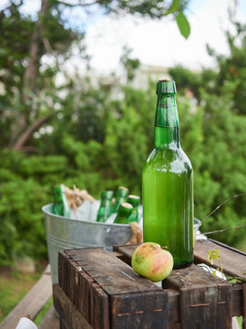 Bottle of Asturian cider (fermented apple juice) traditional drink typical of Asturias region in Spain on top of wooden box with natural apple.Outdoor scene.