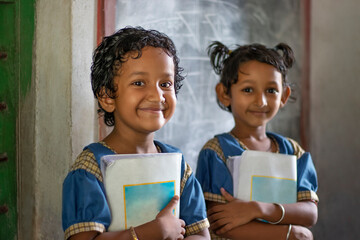 Three School Children's holding books standing at school