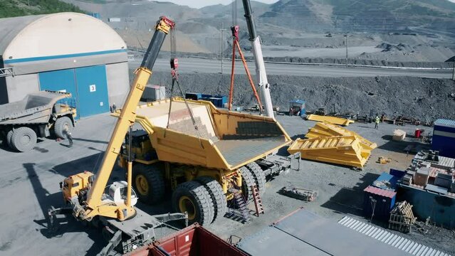 Installation of the body on a dump truck with two cranes. Aerial view.